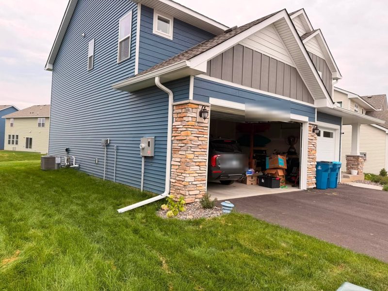 Blue two-story house with a stone-wrapped column, white gutter and a downspout beside the garage