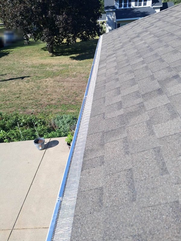 Close view of a gutter with a mesh guard along a grey shingled roof edge, lawn below