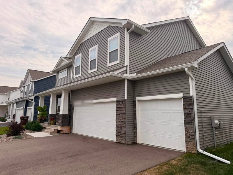 Grey two-story house with two garage doors, white gutters and a white downspout at the corner